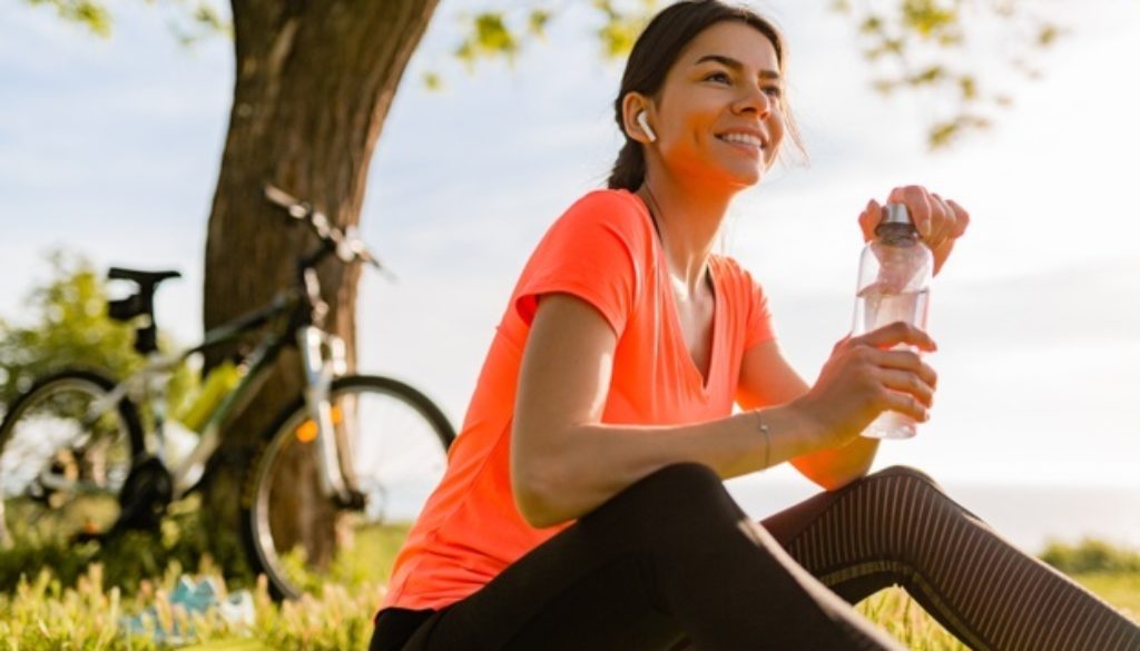 sonriente-mujer-hermosa-bebiendo-agua-botella-haciendo-deporte-manana-parque_285396-4388