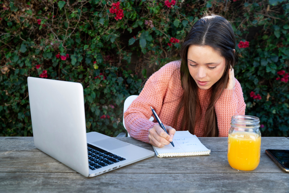 mujer-joven-tomando-notas-al-aire-libre-mientras-usa-computadora-portatil