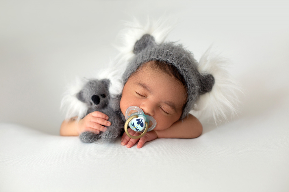 babyboy-recien-nacido-lindo-pequeno-bebe-descansando-sombrero-gris-oso-juguete-gris-mano-chupete-boca-sobre-piso-blanco